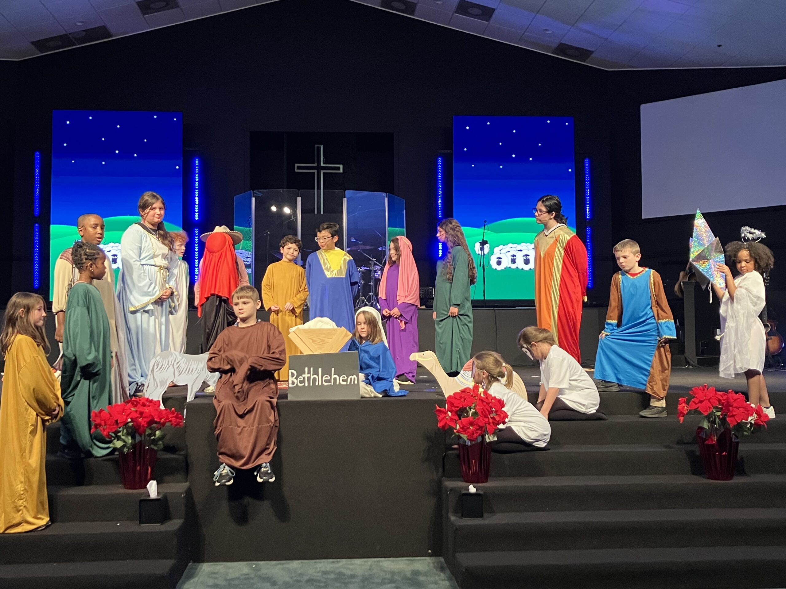 Covington Academy elementary students performing on stage during the Sheep in Heavenly Peace Christmas program, with vibrant costumes and joyful expressions.